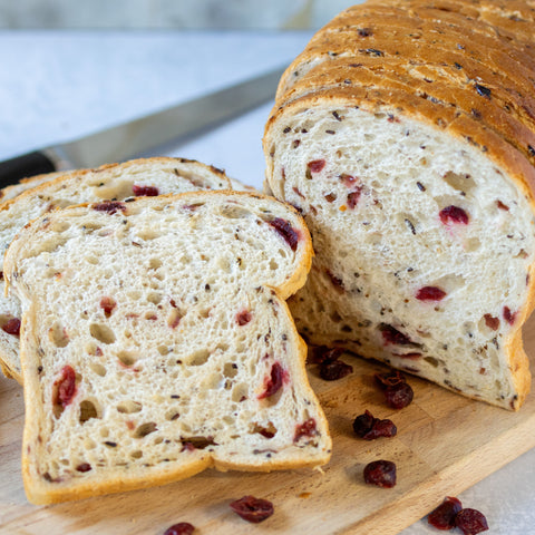 Sliced bread with dried fruits on a wooden board with a knife in the background.