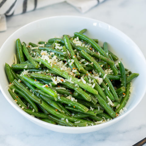 A bowl of green beans topped with parmesan crumb, served on a white plate with a striped napkin beside it.