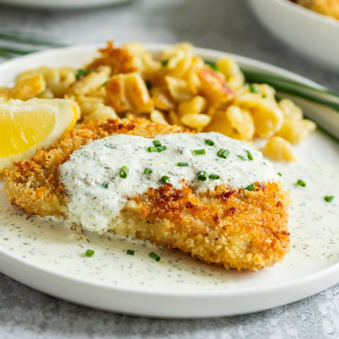 Breaded pork with lemon wedge and creamy sauce on a white plate, served with spaetzle.