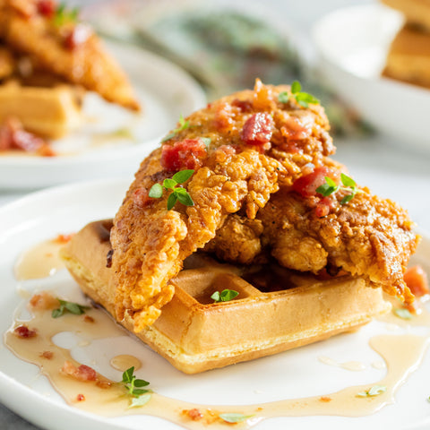 Fried chicken with waffles on a white plate, garnished with herbs.